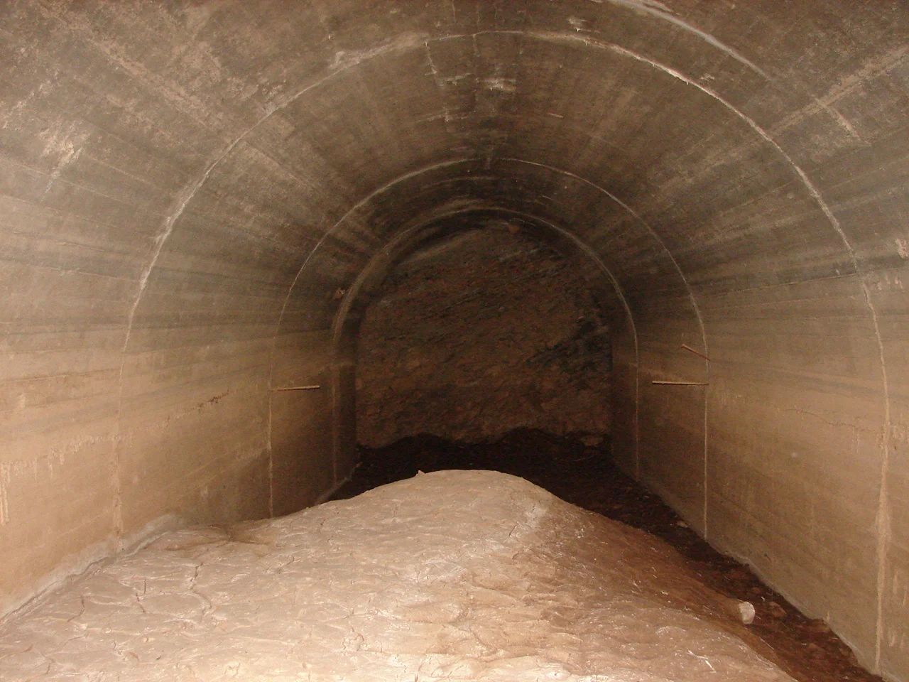 Hex River Tunnel, original eastern portalLocation: Kleinstraat, near Touwsrivier, Western Cape. The tunnel floor has probably been silted up by about 6 to 10 feet since 1950. The floor is cracked silt, dry about halfway in and wet and slippery deeper in. The whole place appears to be under water every rainy season, and the silt has built up considerably over the years.