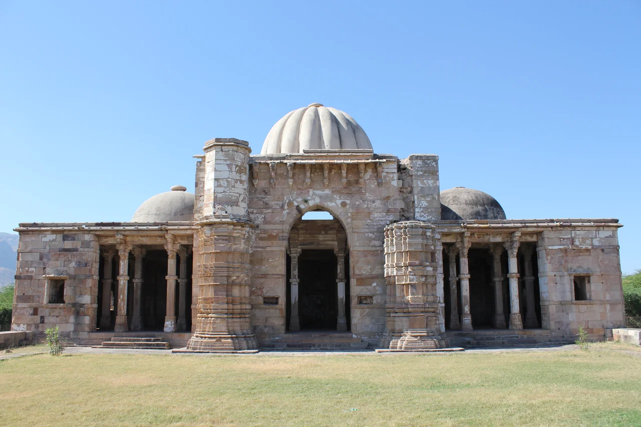 Champaner, Lila Gumbaj Ki Masjid
Champaner, also known as Muhammadabad, is a historical city in the state of Gujarat, in western India. The city was briefly the capital of Gujarat.
It was founded by Vanraj Chavda, the most prominent king of the Chavda Dynasty, in the 8th century. He named it after the name of his friend and general Champa, also known later as Champaraj. By the later 15th century, the Khichi Chauhan Rajputs held Pavagadh fort above the town of Champaner. The young Sultan of Gujarat, Mahmud Begada, deciding to attack Champaner, started towards it with his army on 4 December 1482. After defeating the Champaner army, Mahmud captured the town and besieged Pavagadh, the well-known hill-fortress, above Champaner, where king Jayasimha had taken refuge. He captured the Pavagadh fort on 21 November 1484, after a siege of 20 months. He then spent 23 years rebuilding and embellishing Champaner, which he renamed Muhammadabad, after which he moved the capital there from Ahmedabad. In 1535, after chasing away Bahadur Shah, Humayun personally led some 300 Mughals to scale the fort on spikes driven into rock and stonework in a remote and unguarded part of the citadel built over a precipitous hillside on Pavagadh Hill. Large heaps of gold, silver and jewels were the war booty even though Bahadur Shah had managed to escape to Diu. Champaner is today the site of the Champaner-Pavagadh Archaeological Park, which UNESCO designated a World Heritage Site in 2004.
There are eleven different types of buildings at the UNESCO-protected Champaner-Pavagadh Archaeological Park, including mosques, temples, granaries, tombs, wells, walls, and terraces. The monuments are situated at the foot of and around the Pavagadh Hill. The Baroda Heritage Trust lists 114 monuments in the area, of which only 39 are maintained by the Archeological Survey of India, due to limited funding.
Lila Gumbaj Ki Masjid, built on a high plinth, has a frontage with an arched entrance at the centre flanked by two lateral arches. Initially, three entrances existed on the east, south, and north directions. There are well spaced minarets fashioned with horizontal cornices and mouldings, and decorated niches. Of the three domes, the central one has a fluted design and is colourful. On the north-east corner there is a rectangular ablution tank with a deep drain in front. Inside the mosque, there are three mehrabs in the prayer hall and these are decorated with a central suspended kalash carved with floral motifs.

(source: en.wikipedia.org/wiki/Champaner, en.wikipedia.org/wiki/Monuments_of_Champaner-Pavagadh_Arc..., and en.wikipedia.org/wiki/Lila_Gumbaj_Ki_Masjid,_Champaner)